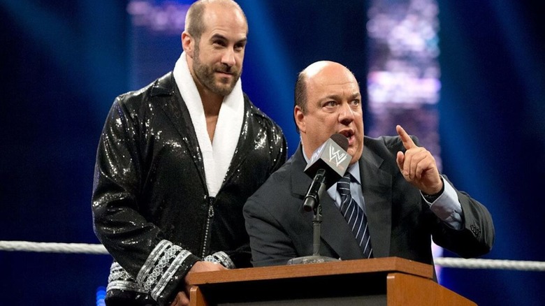 Paul Heyman cuts a promo, flanked by Cesaro, at a podium in the ring during an episode of WWE TV.
