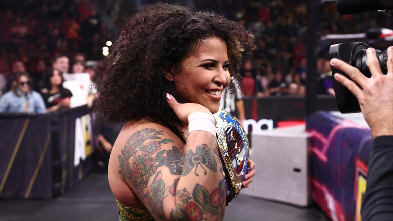 Willow Nightingale is pictured smiling for a camera at ringside, TBS Championship on her shoulder, during an episode of "AEW Collision."