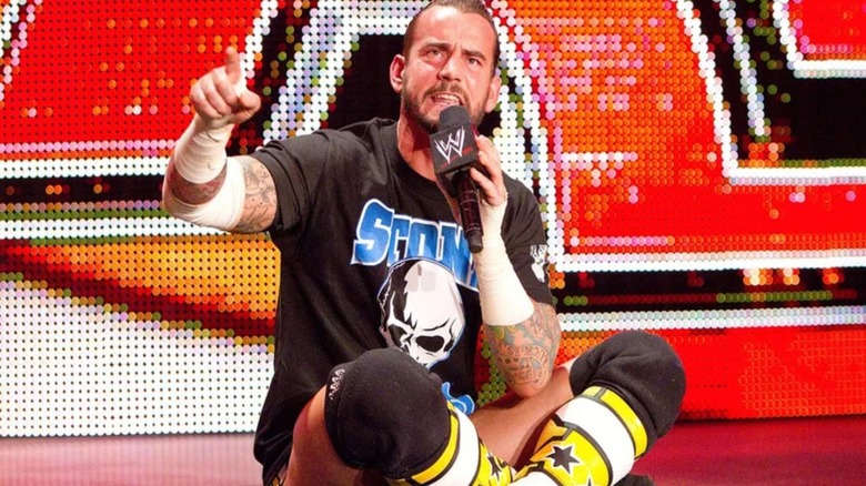 CM Punk sits cross-legged on the stage, microphone in hand, to cut his infamous "pipe bomb" promo on an episode of "WWE Raw."